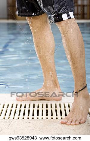 Stock Image - Low section view of a mid adult man standing at the poolside. Fotosearch
