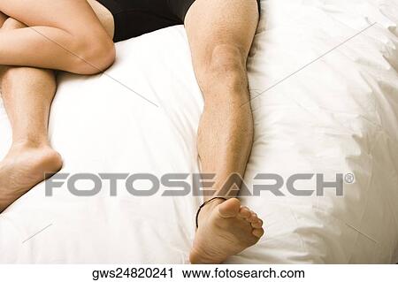 Stock Image - Low section view of a young couple lying on the bed. Fotosearch