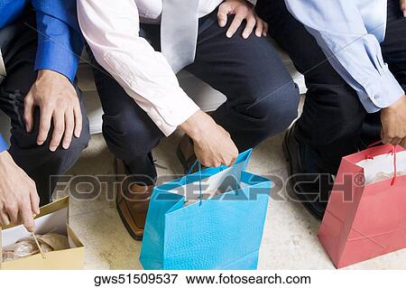 Stock Photo - Low section view of three businessmen sitting with shopping bags. Fotosearch
