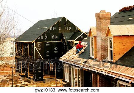 Stock Image - Man putting roof on new home. Fotosearch