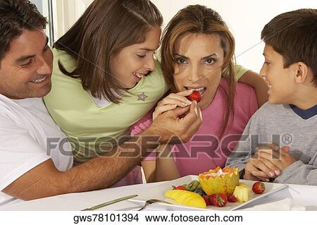 Picture - Mid adult man feeding a mid adult woman a strawberry with their two children beside them. Fotosearch