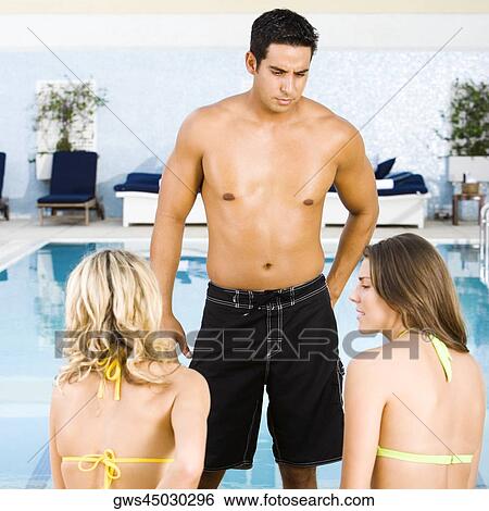 Mid adult man standing in front of two young women at the poolside View Large Photo Image Stock Photograph - Mid adult man standing in front of two young women at the poolside. Fotosearch