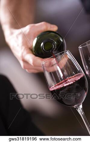 Stock Photograph - Mid section view of a man pouring red wine into a wineglass. Fotosearch