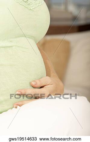 Mid section view of a pregnant mid adult woman touching her abdomen View Large Photo Image Stock Image - Mid section view of a pregnant mid adult woman touching her abdomen. Fotosearch