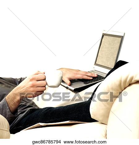 Mid section view of a young man holding a cup of tea using a laptop View Large Photo Image Picture - Mid section view of a young man holding a cup of tea using a laptop. Fotosearch