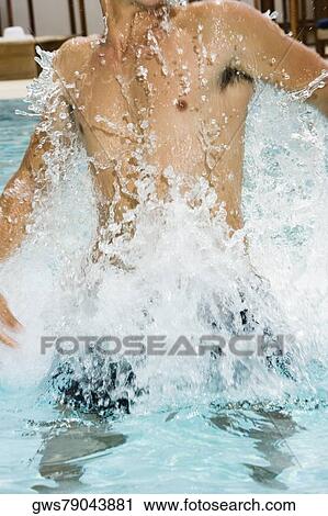 Stock Image - Mid section view of a young man splashing water in a swimming pool. Fotosearch