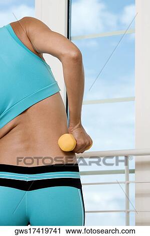 Mid section view of a young woman exercising with a dumbbell View Large Photo Image Stock Image - Mid section view of a young woman exercising with a dumbbell. Fotosearch