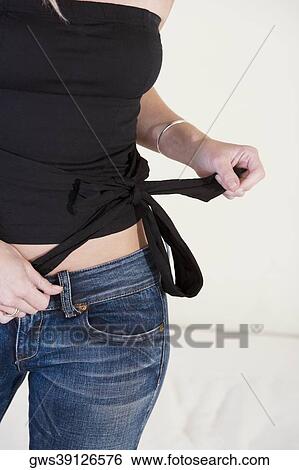 Mid section view of a young woman tying a knot on her top View Large Photo Image Stock Photograph - Mid section view of a young woman tying a knot on her top. Fotosearch