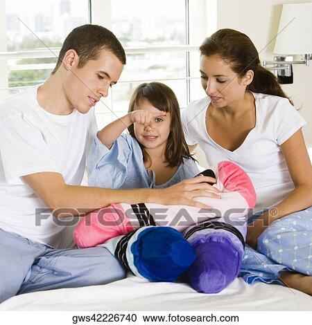 Stock Image - Parents and their daughter sitting on the bed. Fotosearch