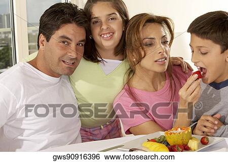 Stock Photograph - Portrait of a mid adult man with his daughter and mid adult woman feeding her son a strawberry. Fotosearch