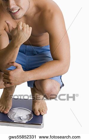 Portrait of a young man crouching on a weighing scale View Large Photo Image Stock Image - Portrait of a young man crouching on a weighing scale. Fotosearch