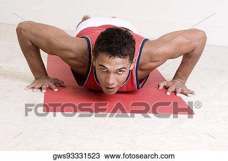 Stock Image - Portrait of a young man doing push-ups on an exercise mat. Fotosearch