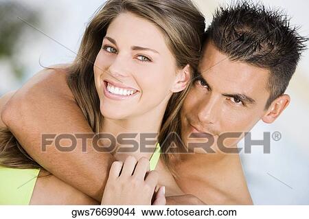 Picture - Portrait of a young man embracing a young woman from behind. Fotosearch