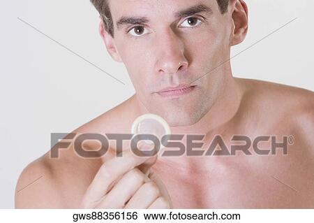 Stock Photograph - Portrait of a young man holding a condom. Fotosearch