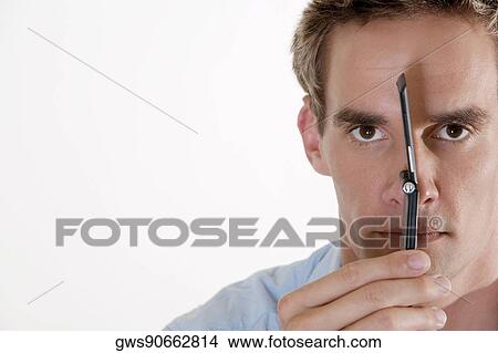 Portrait of a young man holding a mobile phone against his face View Large Photo Image Picture - Portrait of a young man holding a mobile phone against his face. Fotosearch