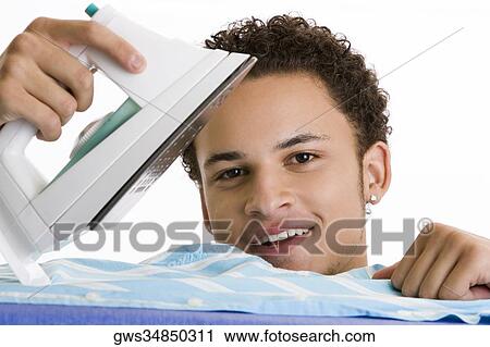 Stock Image - Portrait of a young man ironing his shirt. Fotosearch