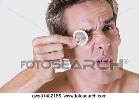 Stock Photography - Portrait of a young man looking through a condom. Fotosearch