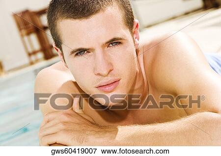 Stock Photo - Portrait of a young man lying at the poolside. Fotosearch