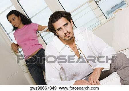 Portrait of a young man sitting on the bed with a young woman standing behind him View Large Photo Image Stock Photo - Portrait of a young man sitting on the bed with a young woman standing behind him. Fotosearch
