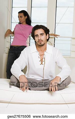 Portrait of a young man sitting on the bed with a young woman standing behind him View Large Photo Image Stock Photograph - Portrait of a young man sitting on the bed with a young woman standing behind him. Fotosearch