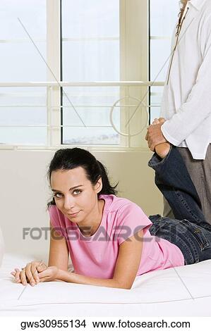 Portrait of a young woman lying on the bed with a young man standing behind her View Large Photo Image Picture - Portrait of a young woman lying on the bed with a young man standing behind her. Fotosearch