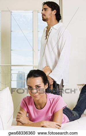 Portrait of a young woman lying on the bed with a young man standing behind her View Large Photo Image Stock Image - Portrait of a young woman lying on the bed with a young man standing behind her. Fotosearch