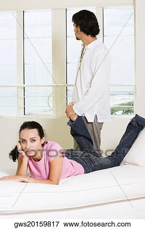 Portrait of a young woman lying on the bed with a young man standing behind her View Large Photo Image Stock Photo - Portrait of a young woman lying on the bed with a young man standing behind her. Fotosearch