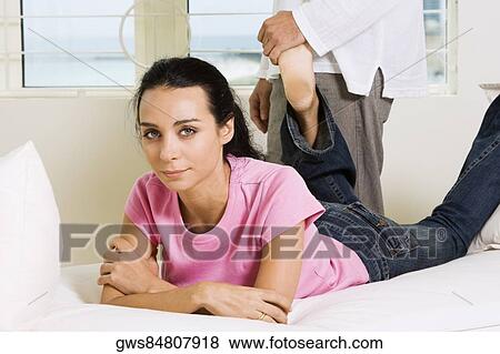 Portrait of a young woman lying on the bed with a young man standing behind her View Large Photo Image Stock Photo - Portrait of a young woman lying on the bed with a young man standing behind her. Fotosearch