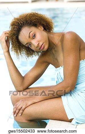 Stock Image - Portrait of a young woman sitting at the edge of a swimming pool with her hand in her hair. Fotosearch