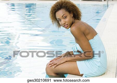 Stock Image - Portrait of a young woman sitting at the edge of a swimming pool. Fotosearch