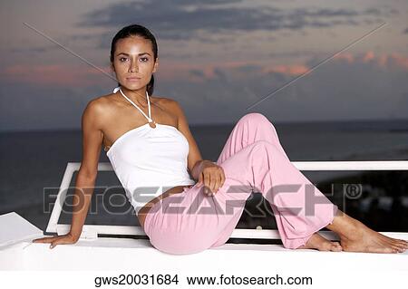 Picture - Portrait of a young woman sitting near the sea at dusk. Fotosearch