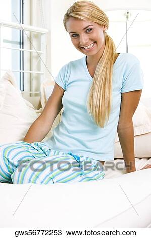 Portrait of a young woman sitting on a bed View Large Photo Image Stock Image - Portrait of a young woman sitting on a bed. Fotosearch