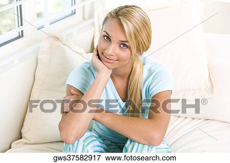 Portrait of a young woman sitting on a bed with her hand on her chin View Large Photo Image Stock Photo - Portrait of a young woman sitting on a bed with her hand on her chin. Fotosearch