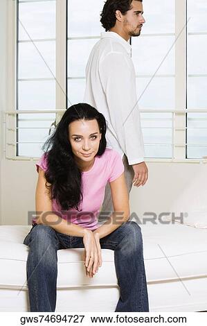 Portrait of a young woman sitting on the bed with a young man standing behind her View Large Photo Image Stock Photo - Portrait of a young woman sitting on the bed with a young man standing behind her. Fotosearch