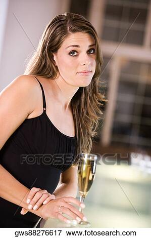 Portrait of a young woman standing at the bar counter holding a champagne flute View Large Photo Image Stock Photo - Portrait of a young woman standing at the bar counter holding a champagne flute. Fotosearch