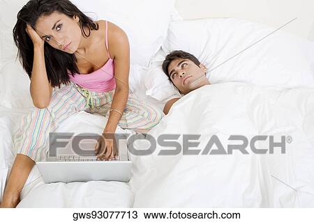 Portrait of a young woman using a laptop with a young man lying beside her View Large Photo Image Stock Image - Portrait of a young woman using a laptop with a young man lying beside her. Fotosearch