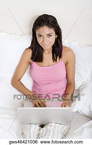 Portrait of a young woman using a laptop in bed View Large Photo Image Stock Photograph - Portrait of a young woman using a laptop in bed. Fotosearch