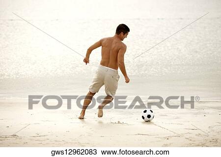Rear view of a mid adult man playing soccer on the beach View Large Photo Image Stock Image - Rear view of a mid adult man playing soccer on the beach. Fotosearch
