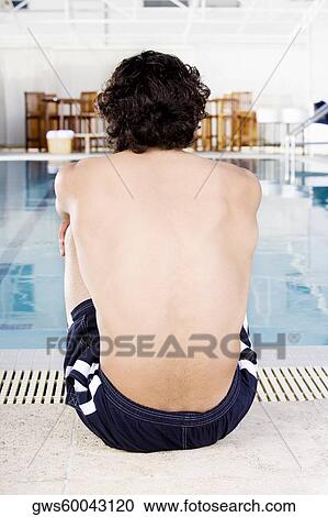 Stock Image - Rear view of a mid adult man sitting at the poolside. Fotosearch