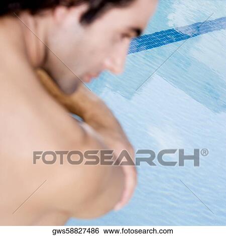 Stock Photograph - Rear view of a mid adult man sitting at the poolside. Fotosearch