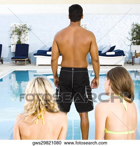 Rear view of a mid adult man standing in front of two young women at the poolside View Large Photo Image Stock Image - Rear view of a mid adult man standing in front of two young women at the poolside. Fotosearch