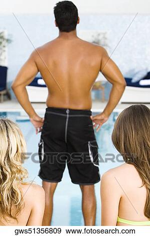 Rear view of a mid adult man standing in front of two young women at the poolside View Large Photo Image Stock Photo - Rear view of a mid adult man standing in front of two young women at the poolside. Fotosearch