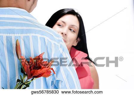 Rear view of a young man standing in front of a young woman with flowers behind his back View Large Photo Image Stock Image - Rear view of a young man standing in front of a young woman with flowers behind his back. Fotosearch
