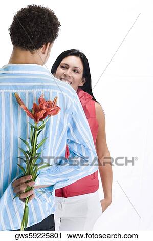 Rear view of a young man standing in front of a young woman with flowers behind his back View Large Photo Image Stock Image - Rear view of a young man standing in front of a young woman with flowers behind his back. Fotosearch