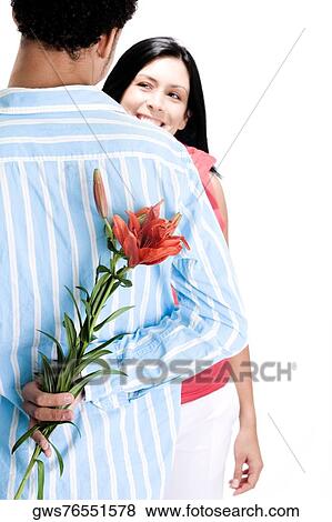Stock Photo - Rear view of a young man standing in front of a young woman with flowers behind his back. Fotosearch