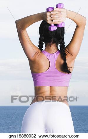 Rear view of a young woman exercising with dumbbells View Large Photo Image Stock Image - Rear view of a young woman exercising with dumbbells. Fotosearch