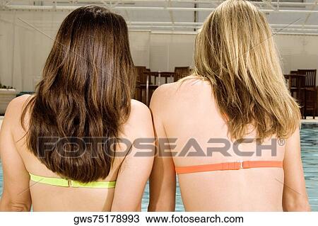 Rear view of two young women sitting at the edge of a swimming pool View Large Photo Image Stock Image - Rear view of two young women sitting at the edge of a swimming pool. Fotosearch