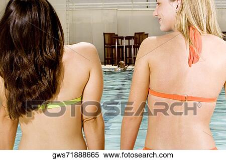 Rear view of two young women sitting at the edge of a swimming pool View Large Photo Image Stock Photography - Rear view of two young women sitting at the edge of a swimming pool. Fotosearch