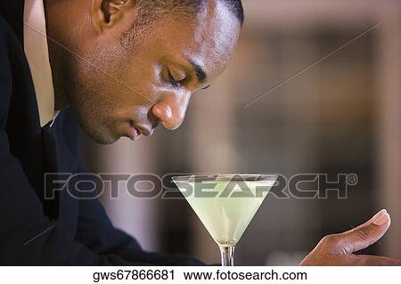 Stock Image - Side profile of a businessman with a glass of martini. Fotosearch