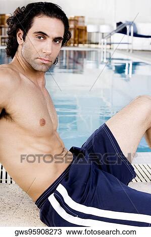 Stock Image - Side profile of a mid adult man sitting at the poolside. Fotosearch